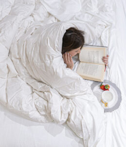 Mujer leyendo bajo un edredon blanco