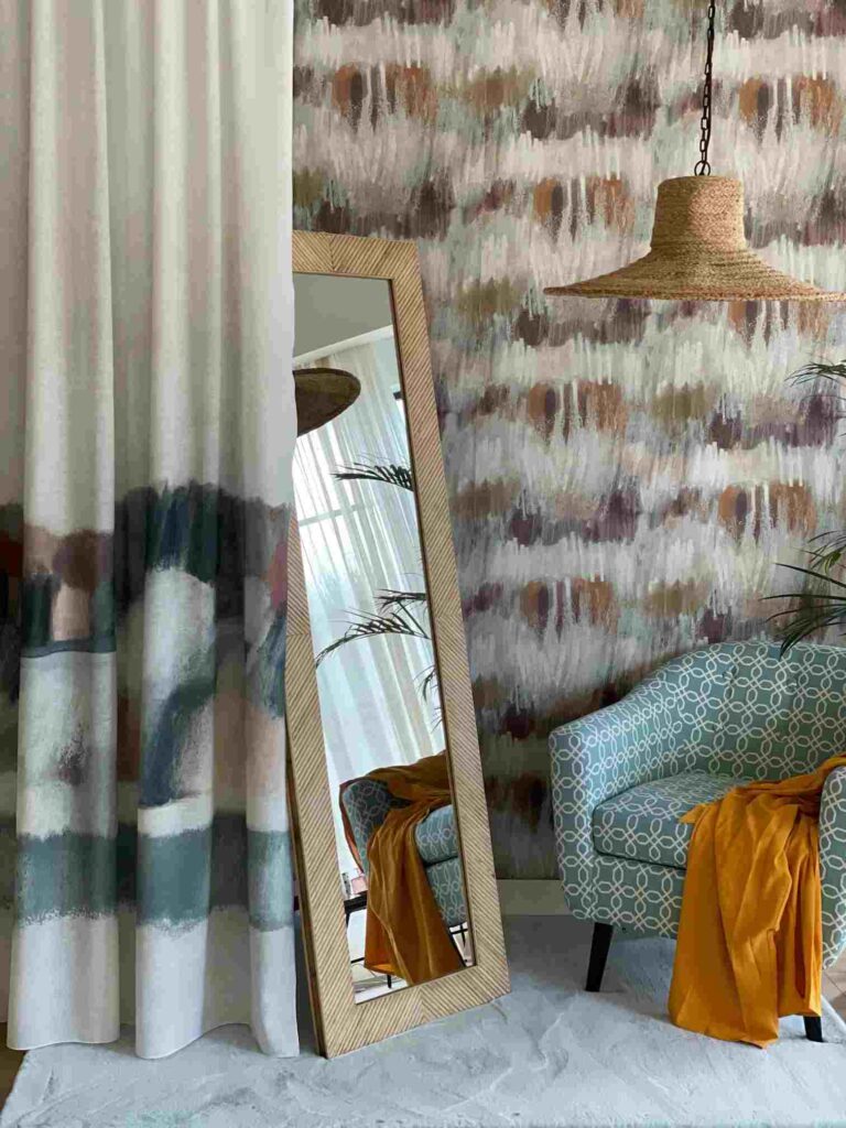 Ambiente compuesto por cortinas estampadas, papel pintado a juego, lampara de yute, butaca verde, espejo y colcha